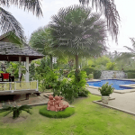 Very nice Pool Villa near Mabprachan lake in best quality and has been well cared by their owners, this quaility property is renovated in 2012. The ground-floors generous living- and dining-area widely opens to the covered-terrace, the pool and gardens and the kitchen is made out of massive teak and so are quite all the built-in. This kitchen is equipped with all the appliances that make cooking joyful and easy plus there is a well-equipped Thai kitchen and also have a laundry room there as well. Outdoors, you get a lavish pool of nearly 100 m2 that is salt-chlorinated also offering an extra Jacuzzi pool plus a waterfall feature. Then the fish pond with beautiful Koi’s swimming. The juicy lawns are easy to maintain as a timer-controlled sprinkler system is in place. The property is surrounded by an attractive natural stone wall. You would access the covered double-carport through a remote-controlled stainless gate. Here we are with the quality features: The whole house is built double cavity and the roof is ventilated. There is ADSL-Internet with Wi-Fi signal all over the property. There are 3 underground freshwater-tanks that are supplied by either your own ground-water or water from the public. There is atmospheric garden lighting and a sound-system installed in the ceilings of the living-area and the terrace. Hot (not just warm) water comes from a central boiler, there are zinc-coated gutters and also an alarm-system installed. A drainage system leads the rain-water underneath the nearby road. All the furniture and equipment seen on the photos stay there. The pool and garden maintenance is included in the rental price.
